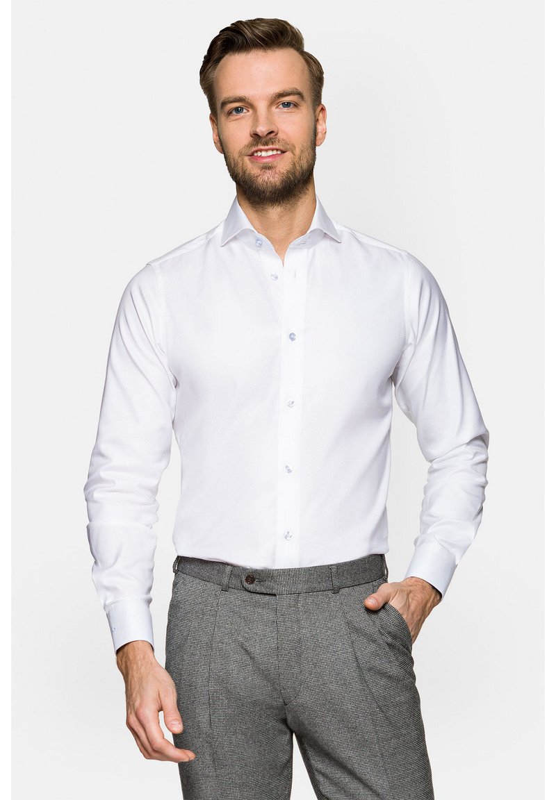 Biała koszula z guzikami przy kołnierzyku, długim rękawem i jasnoniebieskimi guzikami. Noszona z teksturowanymi szarymi spodniami.