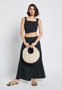 Črn skrajšan top z kvadratnim izrezom, v kombinaciji z dolgo črno krilo z nepravilnimi robovi. Drži okroglo pleteno torbo z bež akcentom.