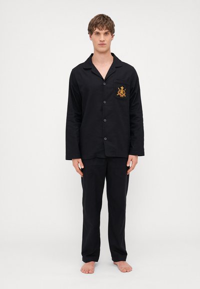 Ensemble de pyjama en coton noir comprenant une chemise à boutons avec une poche et un design brodé, associé à un pantalon ample.