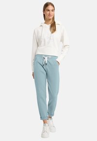 Weißer croppter Hoodie mit helllila Aufdruck, kombiniert mit hellblauen Jogginghosen mit elastischem Bund und umgeschlagenen Bündchen. Weiße Sneakers.