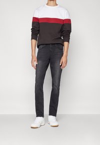 Mørkegrå jeans kombineret med en color-blocked sweatshirt med sektioner i hvid, rød og mørkebrun. Hvide sneakers fuldender outfittet.