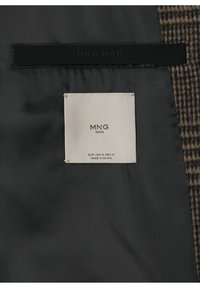 Intérieur en tissu noir d'un vêtement avec une étiquette blanche MNG Man indiquant la taille M et "Made in China" cousue à l'intérieur d'un tissu extérieur marron à carreaux.