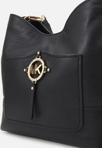 Sac à main en cuir noir avec texture granulée, poche avant, ornement du logo Michael Kors doré et accessoires métalliques.