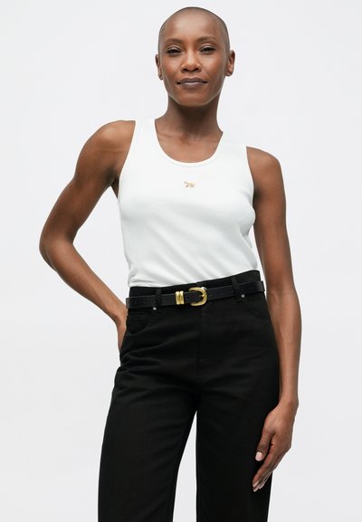 Biely rebrovaný tielko so zlatým zvieracím logom, spárované s čiernymi nohavicami s vysokým pásom a čiernym opaskom so zlatou sponou.