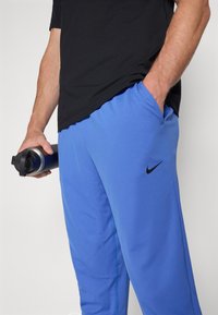 Siniset urheiluhousut, joissa on sileä pinta ja musta Nike-logo. Yhdistetty mustaan t-paitaan; kädessä musta ja hopea vesipullo.