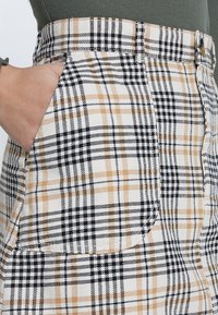 Falda de cuadros de cintura alta en beige, negro y blanco, con un bolsillo en el costado, tela texturizada y un patrón general de cuadros.