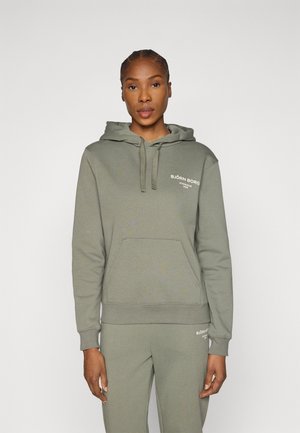 Felpa verde in cotone con tasca frontale, cappuccio con coulisse e logo stampato bianco. Design aderente, abbinata a pantaloni della tuta coordinati.