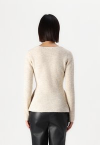 Beżowy sweter w prążki z długimi rękawami i dopasowaną talią. Materiał wydaje się miękki i teksturowany. Widok z tyłu pokazuje skromny dekolt i dół of swetra.