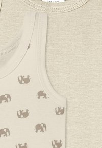 Ljusbeige linne med små bruna elefantmönster, parat med en mjuk beige skjorta med ribbad halsringning.