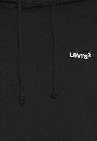 Sudadera negra hecha de tela suave con un bolsillo canguro. Logo bordado en blanco de "Levi's" en el pecho con detalles de cordón en la capucha.