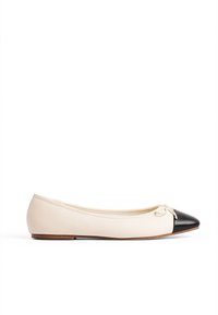 Ballerine en cuir beige avec un bout pointu noir, un accent en nœud sur le devant et une semelle en caoutchouc plate pour un confort optimal.