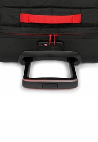 Černý kufr na kolečkách s texturovaným povrchem, červenými zipy a teleskopickou rukojetí integrovanou do černého podstavce.