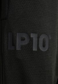 Sort stof med en tekstureret overflade og et stort præget logo "LP10®" i en kontrastfarve i mat sort. Fokus på logoet og tekstildetaljerne.