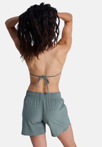Τοπ μπικίνι σε μέντα πράσινο με λεπτές τιράντες που δένονται πίσω, σε συνδυασμό με σορτς με ελαστική μέση στο ίδιο χρώμα, από απαλό, ελαφρύ ύφασμα.