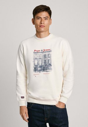 Krémová mikina s grafickým potiskem budovy a nápisem "Pepe Jeans" v červené. Bavlněný materiál, žebrované manžety a volný střih. Viditelné tmavé džíny.