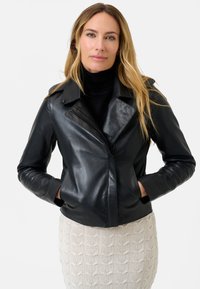 Giubbotto in pelle nera con colletto a revers, zip asimmetrica e due tasche laterali, abbinato a una gonna chiara e strutturata.