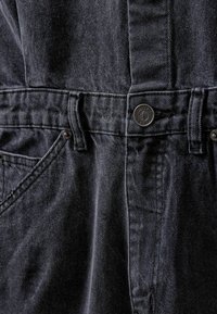 Sötétszürke farmer overall, texturált felülettel, elülső zsebekkel, fém gombos záródással és enyhe fényességgel. Mindennapi viseletre tervezve.