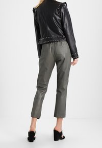 Veste en cuir noire avec épaules volantées et clous en argent. Pantalon en cuir gris au fit décontracté et longueur cropped. Sandales noires à talons épais.