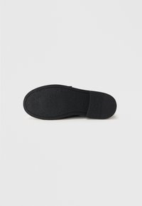 Black shoe sole with a textured surface, featuring a smooth toe area and reinforced heel. No visible branding or accent details.