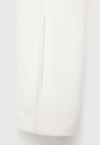 Bela pletenina z rahlo teksturo, ki ima majhen razporek na bočnem robu in urejen šiv ob robovih.