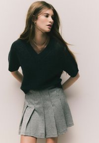 Czarny sweter z krótkim rękawem i dekoltem w serek, w połączeniu z plisowaną spódnicą w czarno-białą kratę houndstooth. Widoczny złoty naszyjnik z łańcuchem.