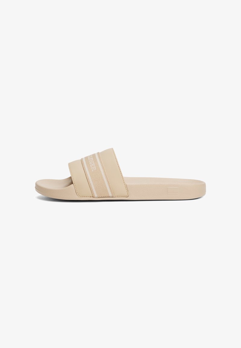 Beige slide sandal made of rubber with a textured sole. Features two horizontal stripes on the strap and logo detailing.