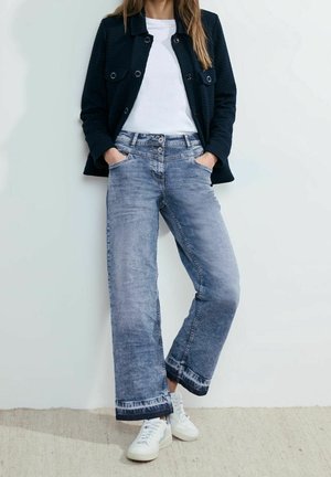 Vaaleanpesuiset farkut leveillä lahkeilla, joissa on rispaantunut helma, yhdistettynä valkoiseen t-paitaan ja teksturoituun mustaan takkiin. Valkoiset tennarit viimeistelevät asun.