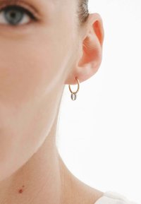 Pendiente de aro dorado con un pequeño acento ovalado. Textura suave, diseño ligero y apariencia simple y minimalista.