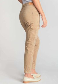 Pantalones cargo beige con un ajuste slim, que cuentan con bolsillos laterales, una tela texturizada y una cintura de altura media. Complementados con mocasines de color claro.