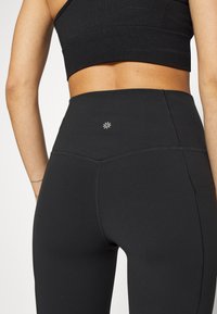 Fekete, magas derékkal rendelkező leggings rugalmas anyagból, kicsi díszítő logóval a derékpánton és lapos varratokkal.