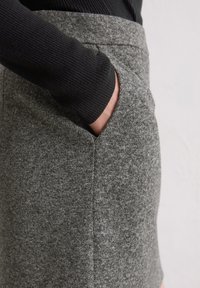 Grauer Wollrock mit strukturiertem Finish, mit Seitentaschen und einem taillierten Bund, Teil eines schwarzen Langarm-Oberteils.