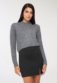 Maglione grigio a maglia con maniche lunghe abbinato a una mini gonna nera a righe verticali con uno spacco laterale. Texture lisce e aderenti.