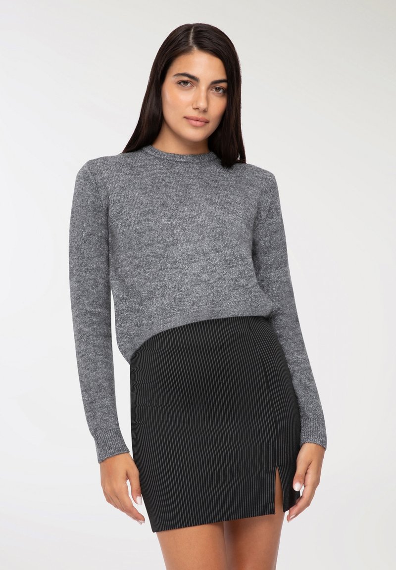 Maglione grigio a maglia con maniche lunghe abbinato a una mini gonna nera a righe verticali con uno spacco laterale. Texture lisce e aderenti.