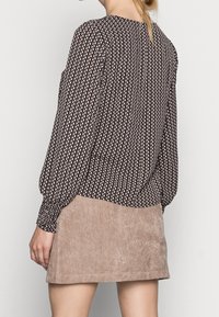 Haut à manches longues marron foncé avec un motif de feuilles, associé à une jupe en velours côtelé beige. Le haut présente des manches froncées et une coupe droite.