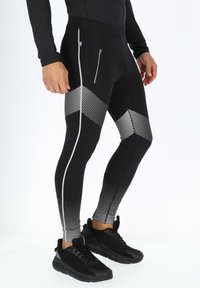 Zwarte sportleggings met een geometrisch zilveren stippenpatroon, een zijvak met rits en een aangesloten ontwerp. Gecombineerd met zwarte sneakers.