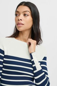 Pull en maille côtelée avec des rayures bleu marine et blanches. Présente un empiècement crème et trois boutons en accent sur la manche. Texture lisse.