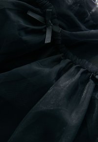 Tessuto di tulle nero con trama arricciata e dettagli in nastro di raso. Presenta un aspetto morbido e traslucido con una sensazione delicata e leggera.