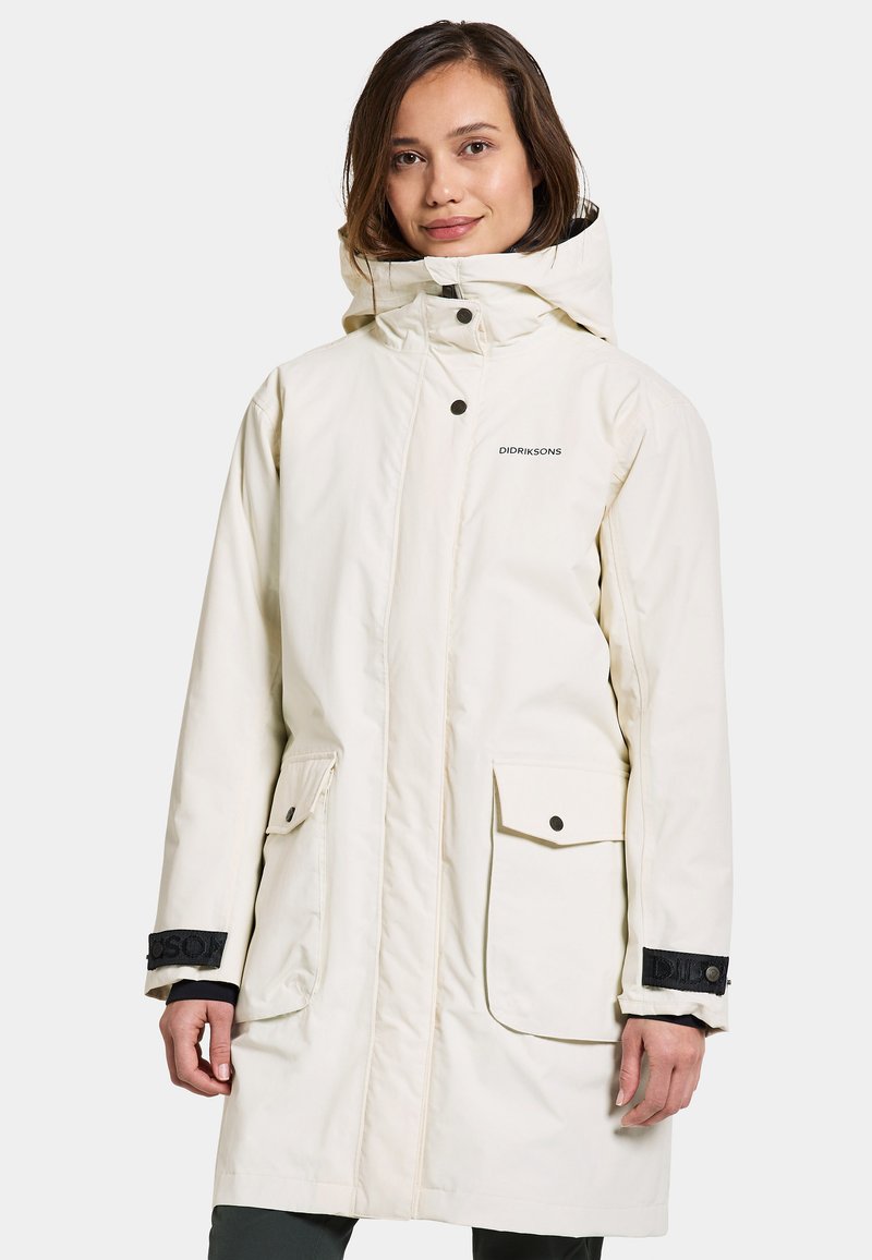 Parka imperméable blanche avec capuche, accents noirs, fermetures à pression et deux poches avant. Texture douce, design longueur genou.