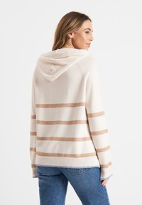 Beżowy sweter w paski z kapturem, o miękkiej teksturze, z jasnobrązowymi paskami, ściągaczami na rękawach i lekko luźnym kroju. Wyświetlony widok z tyłu.