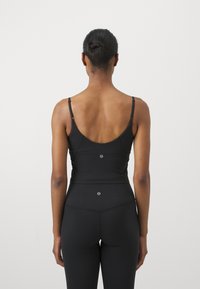 Camiseta deportiva negra sin mangas con tirantes finos, un corte amplio en la espalda y un diseño ajustado. El material parece elástico y suave. Acentuada con detalles del logo.