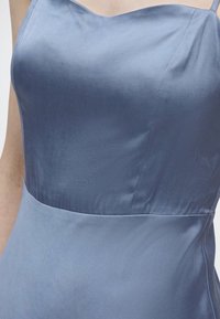 Κοντινό πλάνο ενός ατόμου που φοράει ένα αμάνικο ανοιχτό μπλε σατέν φόρεμα με εφαρμοστό μπούστο και ορατές λεπτομέρειες ραφών.