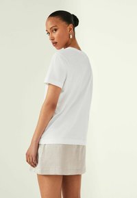 Chemise blanche à manches courtes avec un col rond, associée à une jupe en lin gris clair, présentant une texture lisse et une coupe décontractée.