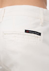 Witte katoenen broeken met een achterzak met een zwart label waarop "CIPO & BAXX" staat. Soepele textuur en slim fit.