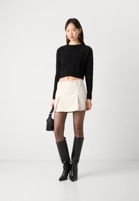 Svart kortärmad tröja med ribbad textur, krämfärgad plisserad minikjol, genomskinliga svarta strumpbyxor och knähöga svarta stövlar. Liten svart väskaccessoar.