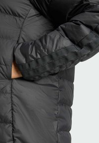 Crna puf jakna s kvadratnim uzorkom, koja se ističe glatkom teksturom i bočnim džepovima. Osvježena crnim horizontalnim trakama na rukavima.