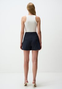 Top in cotone bianco a costine abbinato a pantaloni corti blu a righe. I pantaloni hanno una vestibilità rilassata, una texture liscia e una vita elastica.