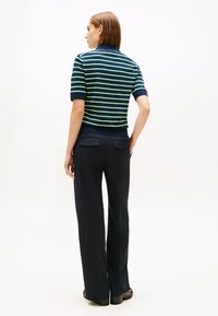 Pull-over à manches courtes rayé bleu marine et vert avec col côtelé, associé à un pantalon noir ajusté doté de deux poches arrière.