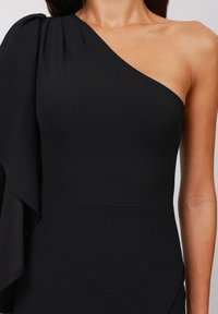 Svart one-shoulder klänning i mjukt, elastiskt material. Har en draperad ärm med rynkade detaljer och en figurnära silhuett.
