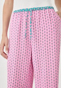 Różowe spodnie w wzory z elastycznym paskiem ściągającym i turkusowym akcentem. Wzór zawiera drobne kwiatowe motywy na całej powierzchni materiału.