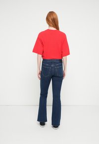 Camiseta roja de gran tamaño con mangas cortas combinada con vaqueros acampanados azules. La modelo lleva zapatillas negras, mostrando un look casual y relajado.